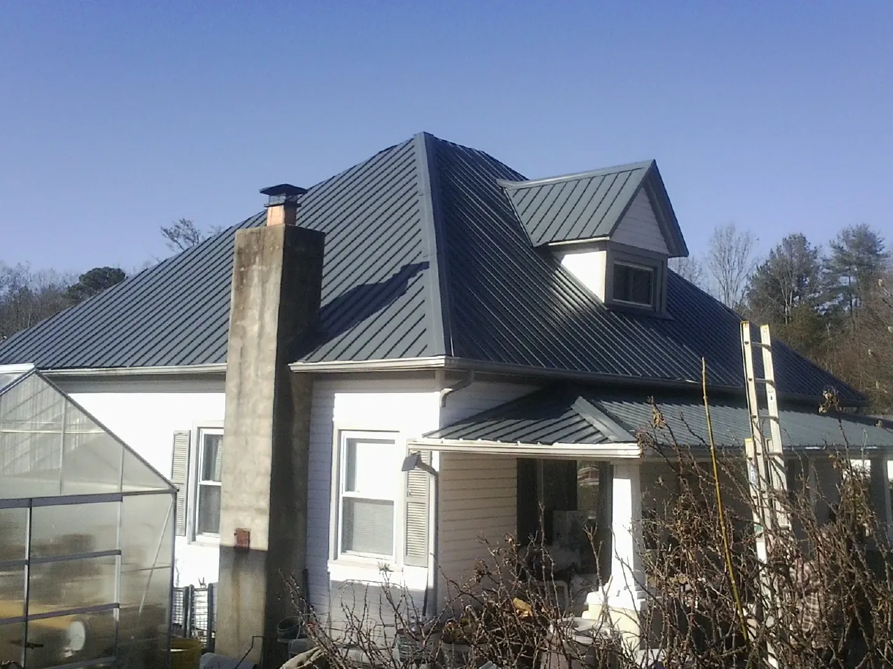 Dark blue standing seam metal roof on a white farmhouse with dormer — Slate & Tile Roof Repair by Roofing Brothers in Picabo