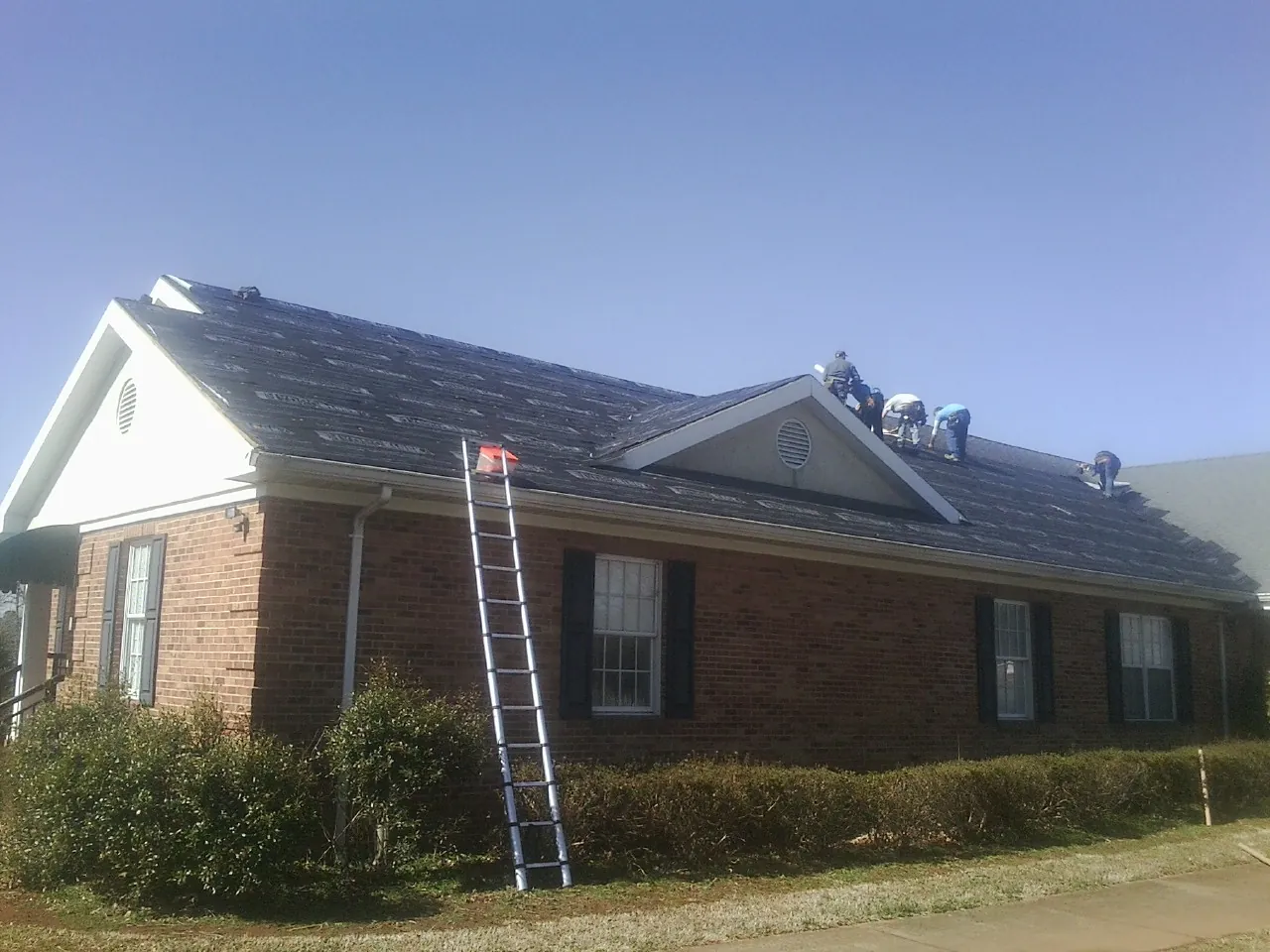 Crew tearing shingles off a brick ranch roof with a ladder set — Metal Roof Repair work by our crew in Picabo