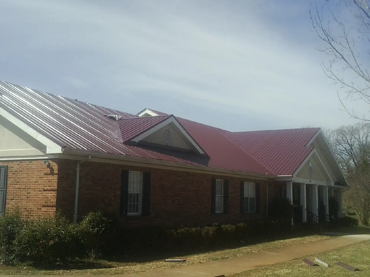 Red metal roof with gabled entries on a long brick building, from a Hail Damage Roof Repair job in Picabo