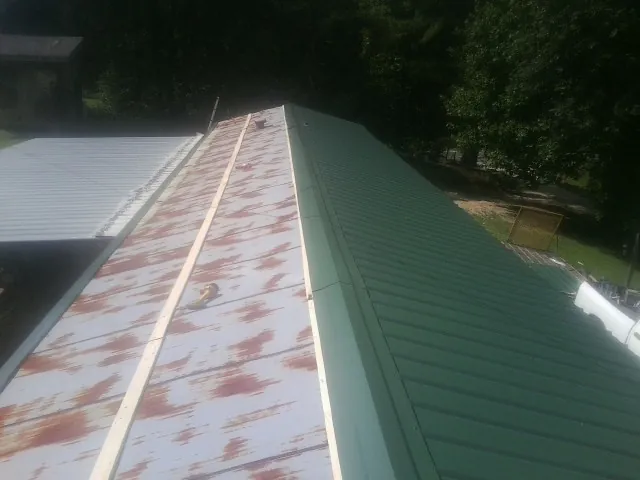 Old rusted panels beside newly installed green metal roofing — Wind Damage Roof Repair by Roofing Brothers in Picabo