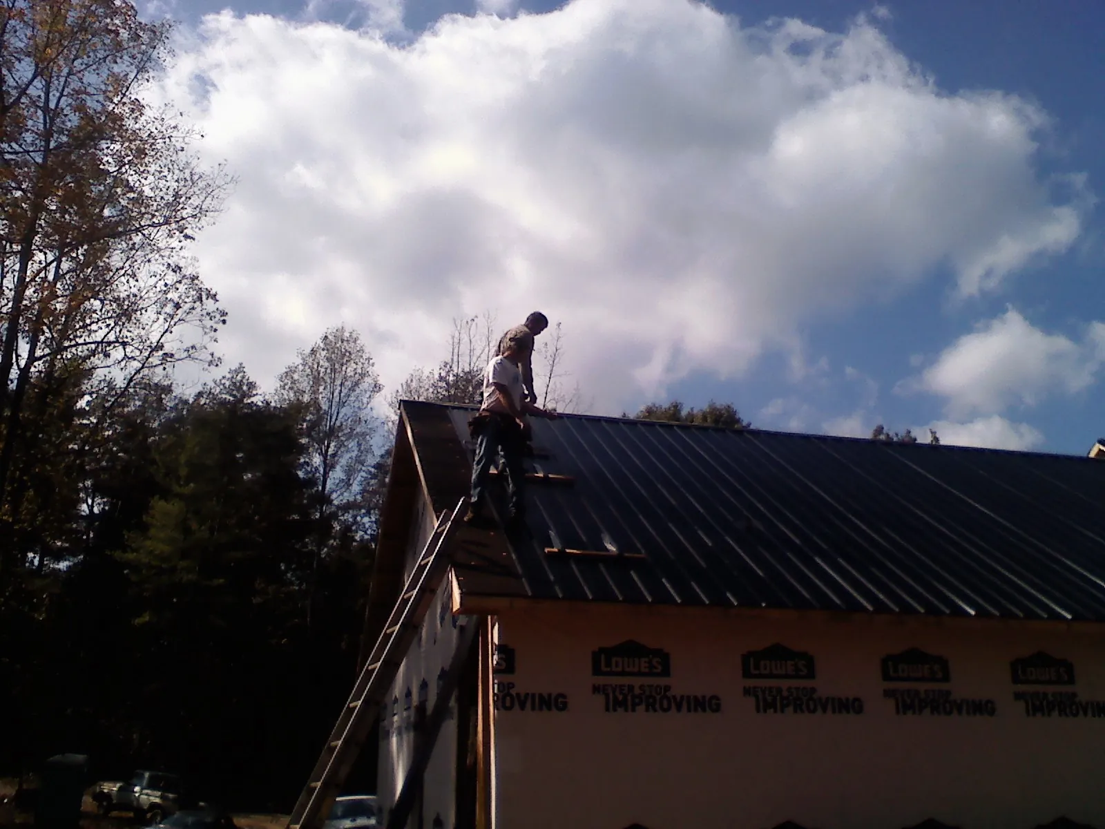 Roofer fastening dark metal panels high against a cloudy sky, from a Roof Inspection job in Picabo